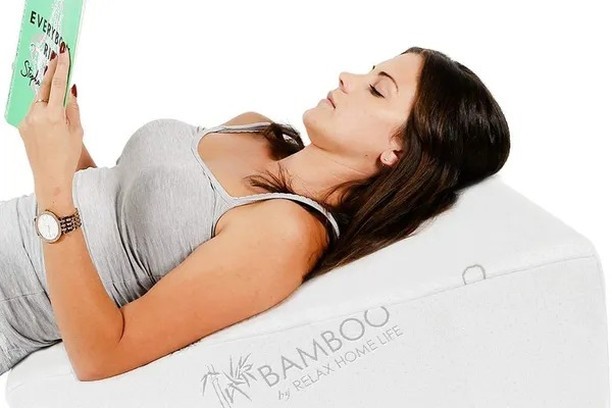 A woman lays on a very tall pillow reading a book. The Relax Home Life 7.5 Inch Bed Wedge PIllow is the best wedge pillow in 2022.